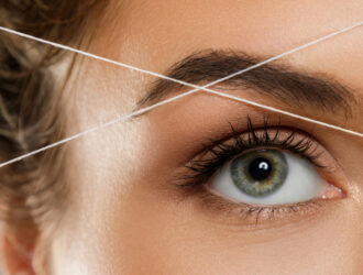 Close-up of female eye with a thread. Eyebrow threading - epilation procedure for brow shape correction