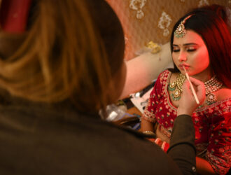 A young Indian bride getting makeup applied for a traditional Indian wedding ceremony.