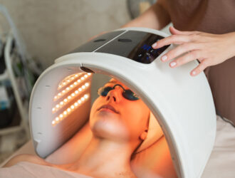 Young woman enjoying LED light therapy for facial skin care, receiving treatment from a skilled beautician in a relaxing spa environment